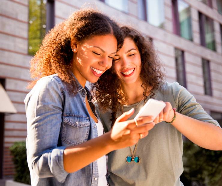 Two women looking at one's smartphone. Appearing happy, pointing at the screen.